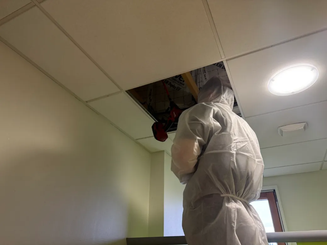 Technicien dépoussiérant un conduit de ventilation en faux plafond dans un établissement scolaire